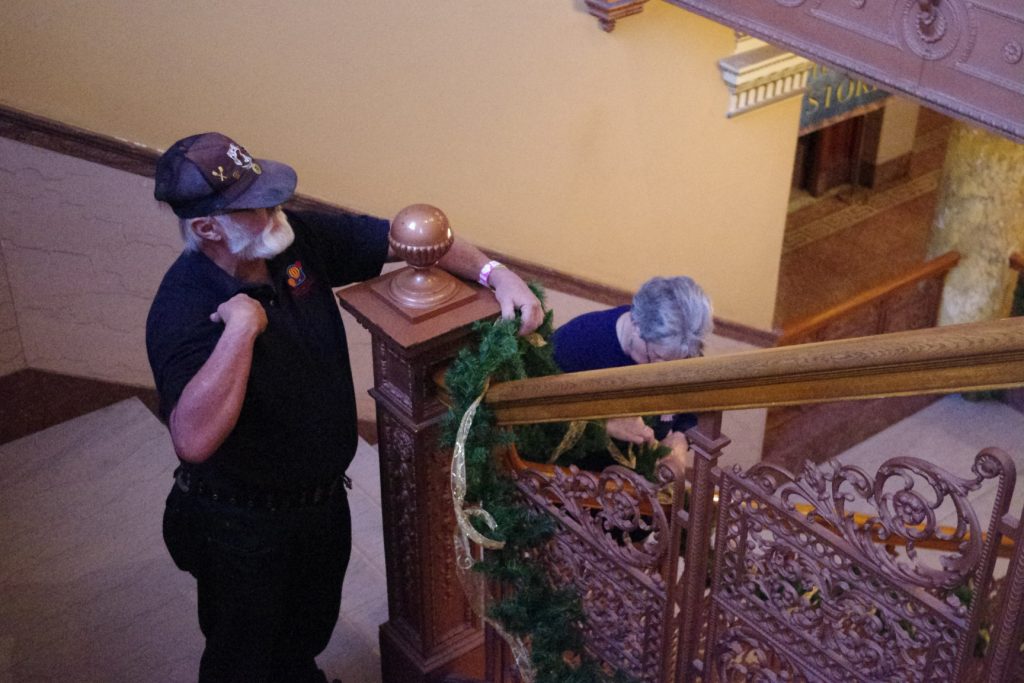 Larry Schaefer helps another volunteer place an evergreen garland along the bannister of a stairwell in the Museum.