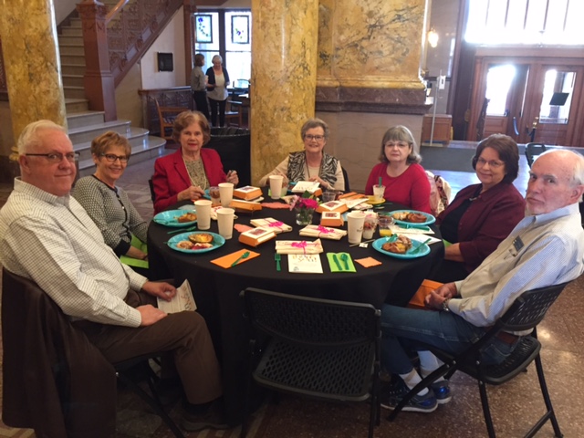 A group of CSPM Volunteers are seated around a table in the foyer of the Museum