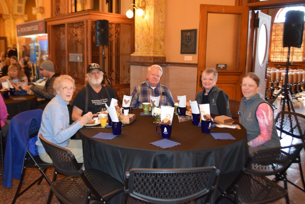 CSPM Volunteers are seated around a table set in the lobby of the museum.
