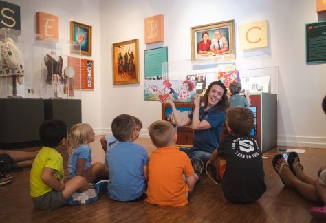 Image of young children sitting in a circle being read to by an adult.