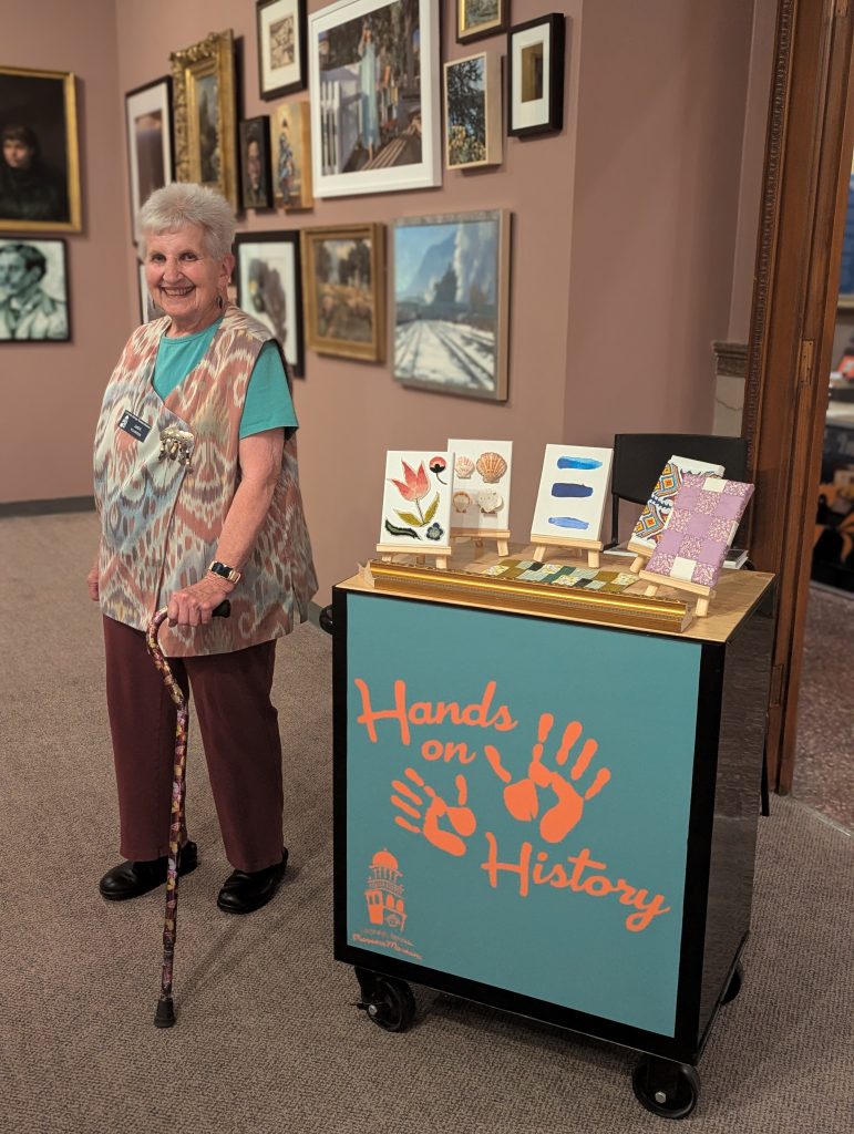 Gallery Attendant standing next to the Hands on History cart.