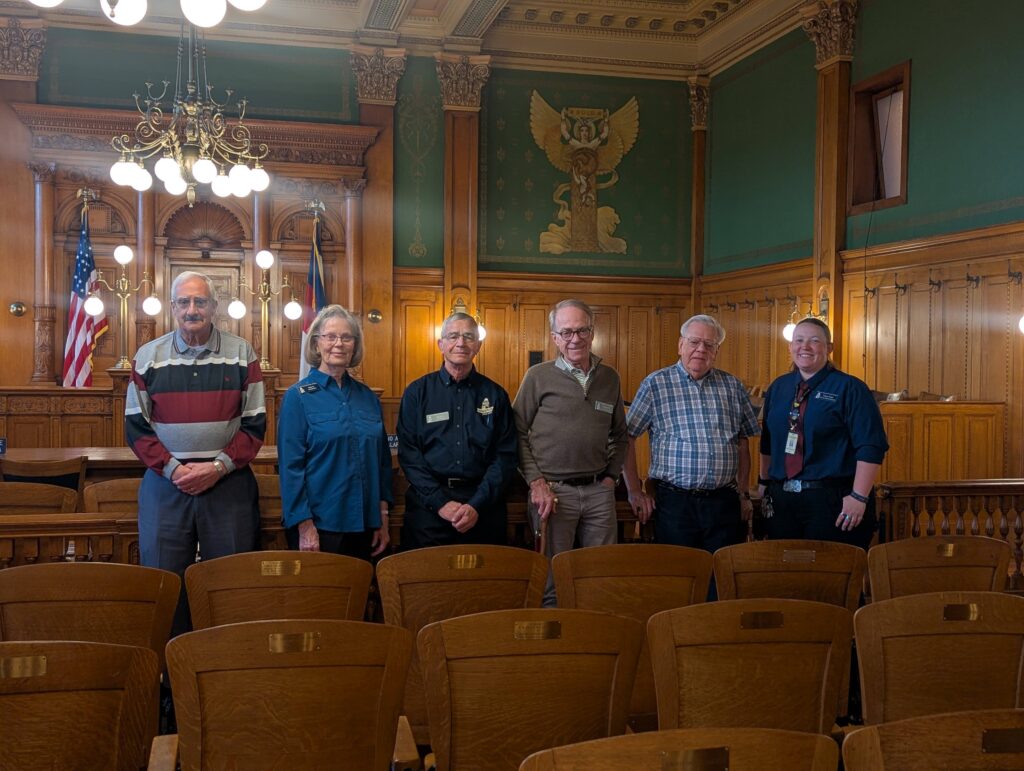 A group of front desk volunteers poses for a photo in the museum's Division 1 Courtroom.
