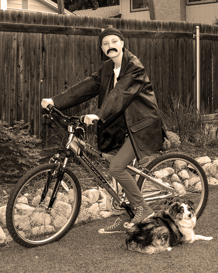 Mars Kelly poses in a black and white photo on a bike next to a dog.