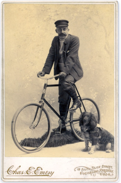 Man on a bicylce next to a dog laying on the ground