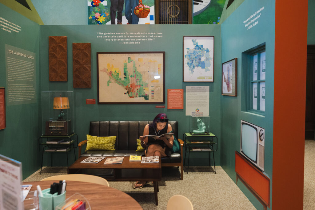 Visitor sitting on a couch and reading an article in the Freedom to Thrive exhibit.