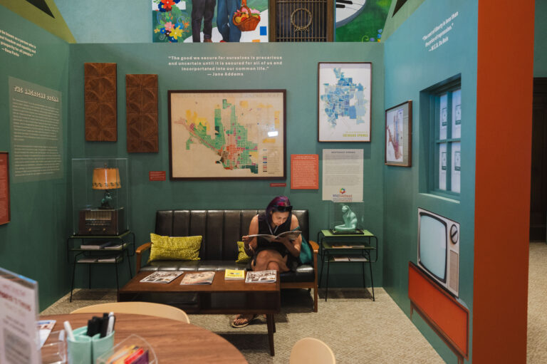 Visitor sitting on a couch and reading an article in the Freedom to Thrive exhibit.
